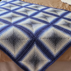 Op de afbeelding: Een gehaakt deken met een ruitpatroon in tinten blauw en wit.