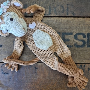 May include: A crocheted monkey toy with a flower crown, brown and beige fur, and a small pink heart on its chest.