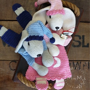 May include: Two crocheted stuffed animals wearing pajamas and nightcaps. The animal on the left is wearing blue pajamas and a blue and white nightcap. The animal on the right is wearing pink pajamas and a pink nightcap. Both animals have white fur and black noses. The animal on the right is holding a small red ornament that says "Best Friend".