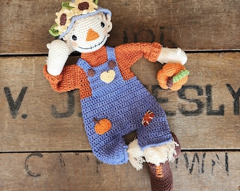 May include: A crocheted scarecrow doll with a sunflower hat, orange and blue overalls, and a small pumpkin in its hand.