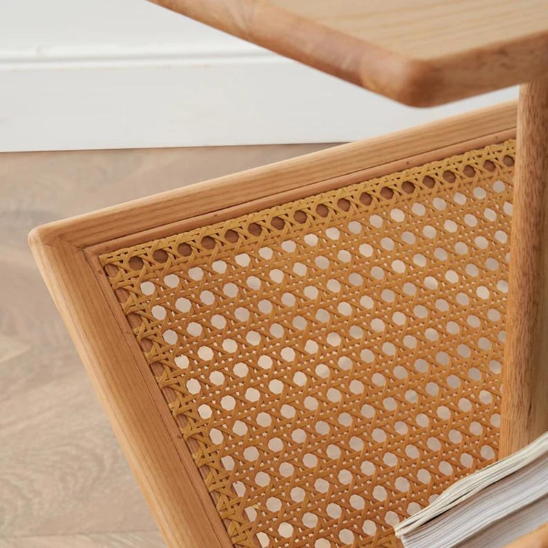 May include: A wooden magazine rack with a woven cane shelf. The rack has a square shape and a natural wood finish.