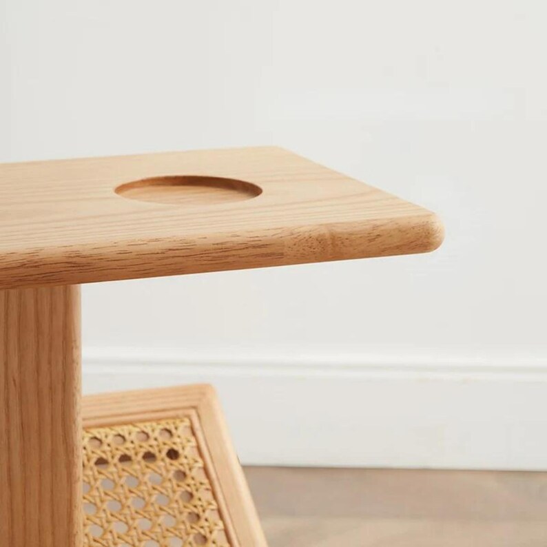 May include: A wooden side table with a round cutout on the top surface and a woven rattan shelf below.