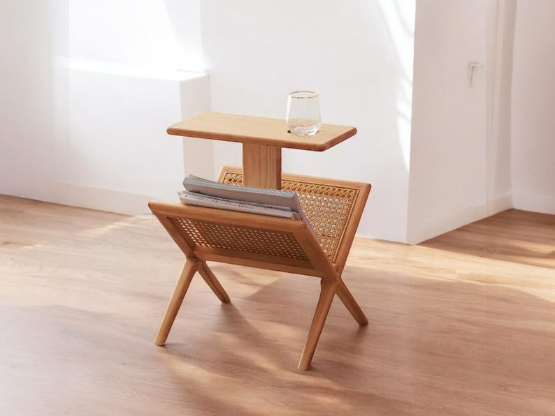 May include: A wooden magazine rack with a woven cane shelf and a small wooden shelf on top. The rack is made of natural wood and has a simple, modern design.
