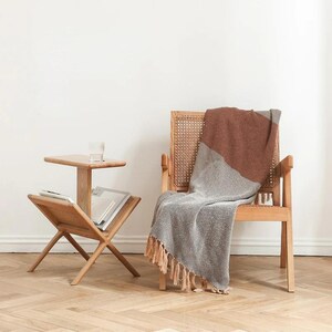 May include: A wooden side table with a magazine rack and a top shelf. A woven chair with a brown and gray throw blanket is in the background.