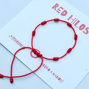 May include: Red string bracelet with knots, made by hand. The bracelet is tied with a slip knot and has a long tail that can be adjusted to fit any wrist size. The bracelet is on a white card with the text "RED HILOS" and "HECHO A MANO".