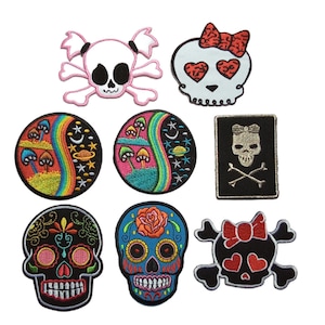 May include: Set of 8 embroidered iron-on patches featuring various skull designs. The patches include a skull with a pink bow, a skull with rainbow eyes, a skull with a flower, a skull with a rainbow and mushrooms, and a skull with a black bow.
