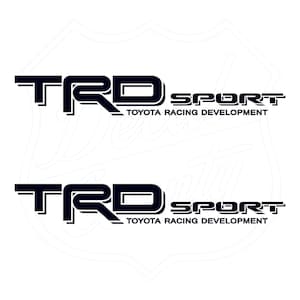 Peut inclure: Deux autocollants noirs et blancs avec le texte "TRD SPORT TOYOTA RACING DEVELOPMENT" dans une police de caractères audacieuse et en blocs.