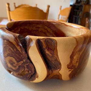 May include: A large, wooden bowl with a natural, rustic finish. The bowl has a unique, irregular shape and is made from a light-colored wood with dark brown streaks.