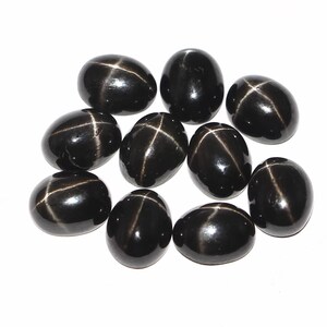 Pode incluir: Dez pedras preciosas cabochão pretas em forma de estrela com um padrão de estrela branca. As pedras são de forma oval e têm um acabamento brilhante.