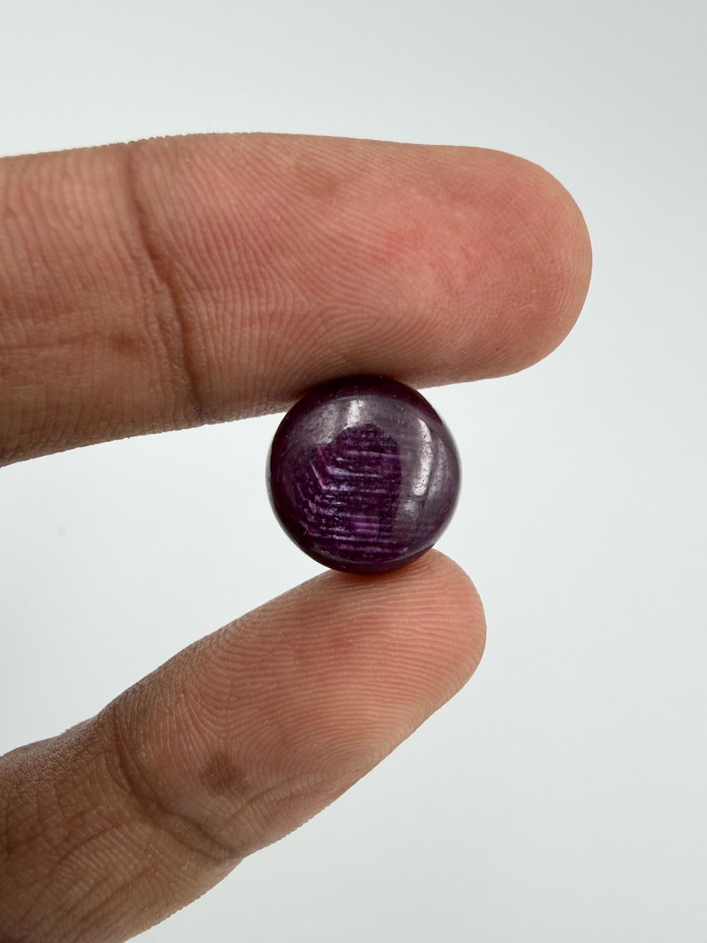 Pu&ograve; includere: Una piccola pietra preziosa rotonda tagliata a cabochon con una tonalit&agrave; profonda e satura di viola scuro e magenta. La superficie della pietra presenta una finitura liscia e lucida con striature interne e inclusioni naturali visibili.