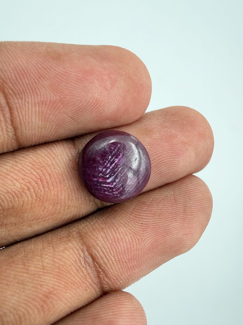 Pu&ograve; includere: Una pietra preziosa di rubino a taglio cabochon rotondo con una profonda tonalit&agrave; rosso violaceo. La pietra mostra un distinto fenomeno ottico a forma di stella noto come asterismo, con raggi di luce che si incrociano sulla superficie.