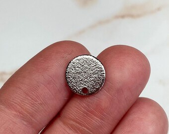 May include: Silver circle charm with a textured surface and a small hole at the top.