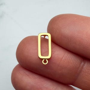 May include: A gold-toned metal earring component featuring a hollow rectangular frame with a small circular jump ring attached to the bottom edge, designed for jewellery making and assembly of dangling accessories.