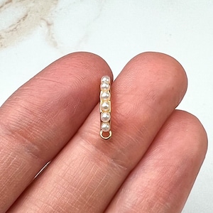 Puede incluir: Encanto dorado con una fila de pequeñas perlas blancas. El encanto tiene un bucle en la parte inferior para sujetarlo a un collar o pulsera.