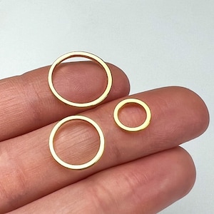 May include: Three gold-colored metal rings of different sizes. The rings are arranged in a row, with the largest ring on the left and the smallest ring on the right.