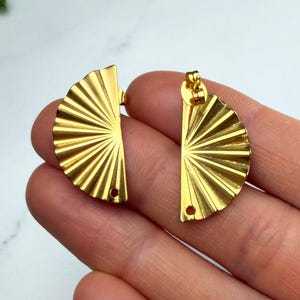 May include: Two gold-colored metal fan-shaped charms with a ribbed, sunburst texture. Each piece features a small circular hole at the bottom edge for attachment, showcasing a polished, reflective finish on the curved, semi-circular design.