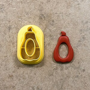 May include: Two cookie cutters shaped like pears. One is yellow plastic and the other is red plastic.