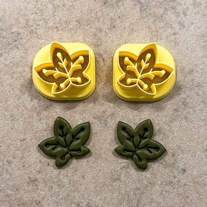 May include: Two yellow plastic leaf-shaped cookie cutters and two green leaf-shaped cookies.