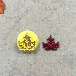 May include: Two leaf-shaped cookie cutters, one yellow and one red, on a gray background.