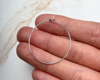 May include: Silver hoop earrings with a simple, circular design. The earrings are shown on a hand, with the hoop held up for viewing.