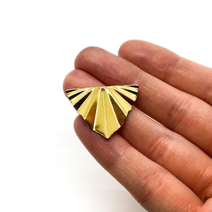 May include: Gold-toned metal pendant with a fan-shaped design. The pendant has a small hole at the top for attaching a chain or cord.
