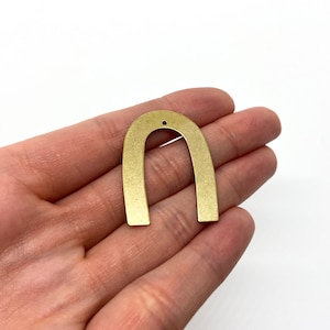 May include: A gold-toned metal arch shape with a small hole at the top. The arch is about 2 inches tall and 1 inch wide.