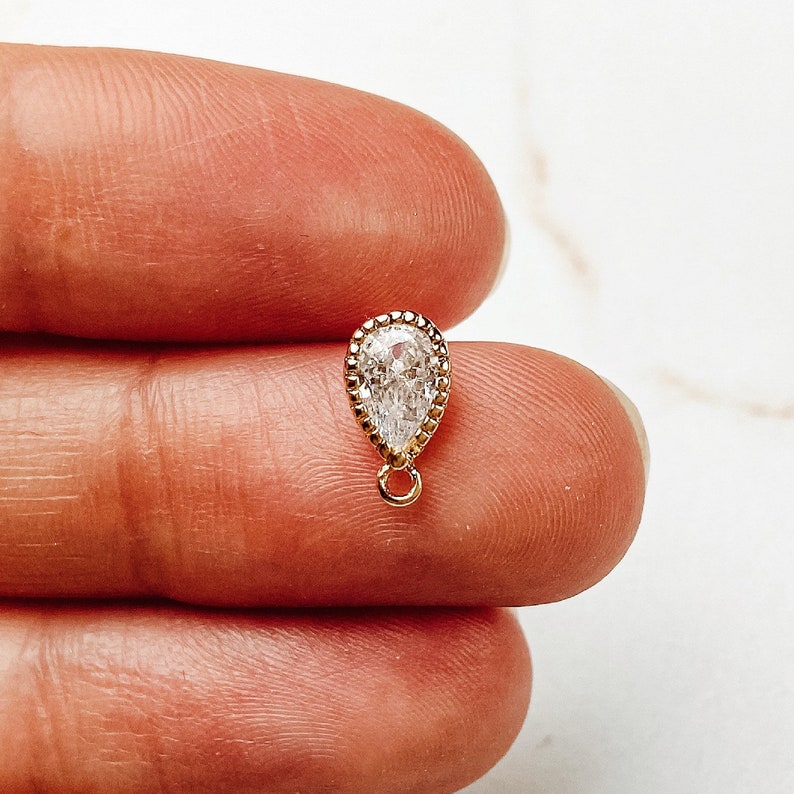 May include: A gold-toned teardrop-shaped pendant with a clear crystal stone.