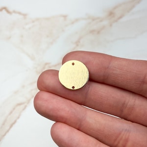 May include: A gold-colored metal circle with two holes. The circle has a textured surface.