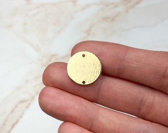 May include: A gold-colored metal circle with two holes. The circle has a textured surface.