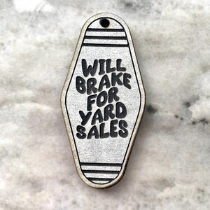 May include: White motel key tag with black text that reads "Will Brake For Yard Sales".
