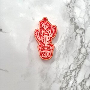May include: Red wooden ornament shaped like a cactus with a zombie face and the text "Zombie Prick".