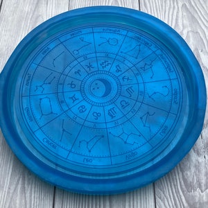 Può includere: Un vassoio circolare blu con un design a ruota zodiacale. La ruota presenta i dodici segni zodiacali e le loro corrispondenti costellazioni. Il vassoio è realizzato in un materiale liscio e lucido.
