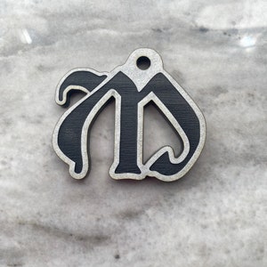 May include: A black wooden ornament shaped like the letter "M" in a stylized font. The ornament has a hole at the top for hanging.