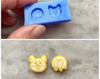 May include: Two yellow resin molds of a cartoon corgi dog, one facing forward and one facing backward. The molds are on a light blue surface.