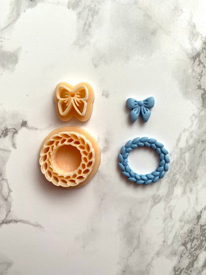 May include: Four cookie cutters: a wreath in a light brown colour, a wreath in a light blue colour, a butterfly in a light brown colour, and a bow in a light blue colour.