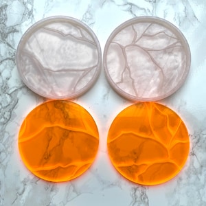 Pode incluir: Quatro  tapetes redondos, dois são brancos com um acabamento rachado e dois são laranja com um acabamento rachado.