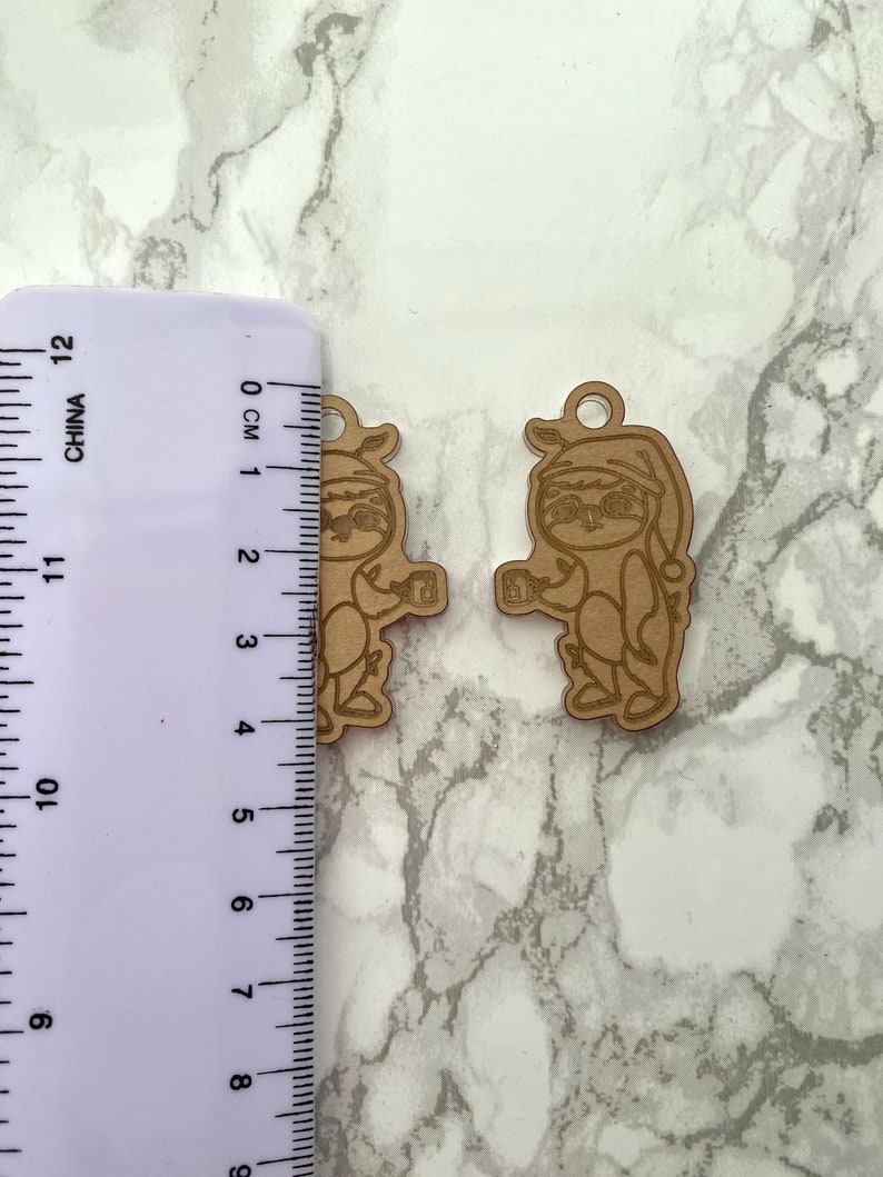 May include: Two wooden ornaments of a sloth wearing a Santa hat and holding a gift. The ornaments are approximately 4 cm tall.