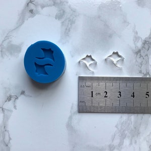 May include: A blue silicone mould with two manta ray shapes. Two clear plastic manta ray shapes are shown next to a ruler measuring 1 cm.