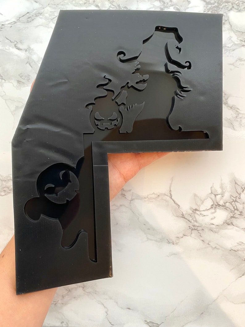 May include: Black acrylic Halloween decoration with a witch, pumpkin, and ghost cutouts. The witch wears a pointed hat and holds a pumpkin. The ghost has a smiling face. The decoration is L-shaped.