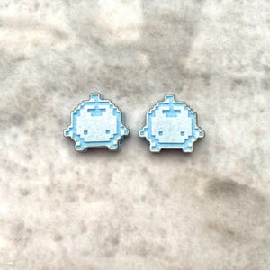 May include: Two light blue pixelated ghost earrings with a white outline.