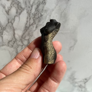 Puede incluir: Una figurita decorativa negra y dorada de un torso humano con detalles intrincados.