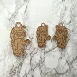 May include: Three wooden ornaments shaped like sloths wearing pajamas and holding mugs. The ornaments are brown and have a rustic look.