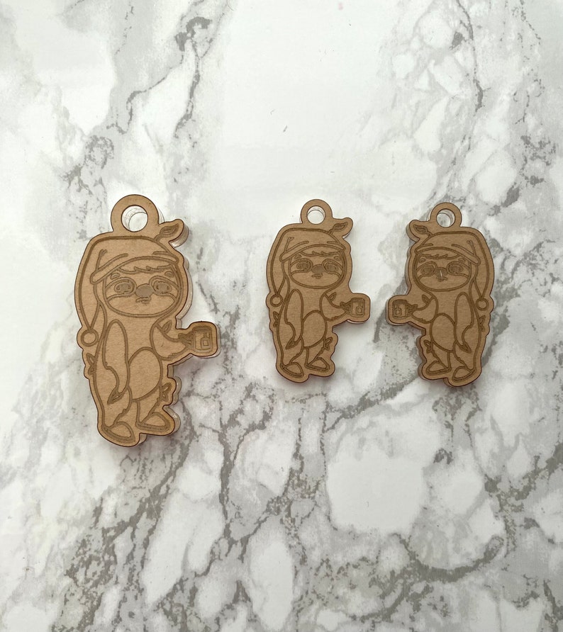 May include: Three wooden ornaments shaped like sloths wearing pajamas and holding mugs. The ornaments are brown and have a rustic look.