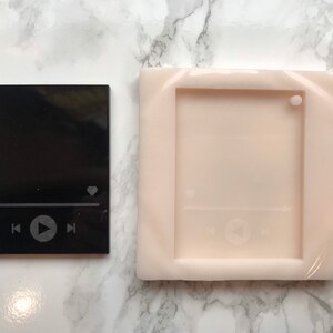 May include: A black and white silicone mold for making a resin keychain. The mold is shaped like a music player with a play button, rewind and fast forward buttons, and a heart icon.