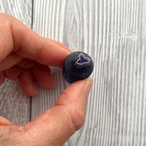 Può includere: Un perno di vetro di colore viola scuro con un disegno bianco al centro.