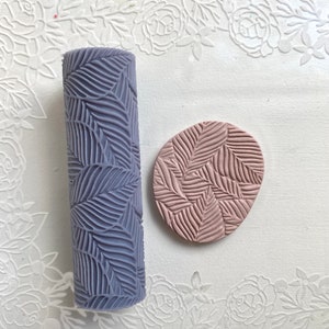 May include: A purple rolling pin with a leaf pattern and a pink clay imprint of the same pattern.