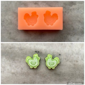 May include: Two green silicone moulds for making chicken-shaped resin earrings. The moulds are on a white surface.