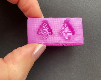 May include: A pink silicone mould with two Christmas tree shapes. The mould is designed for making small resin ornaments or other crafts.