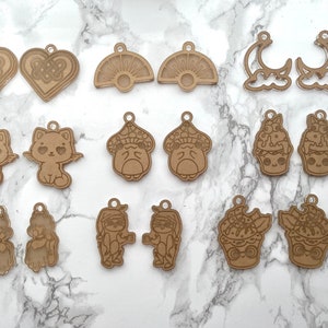 May include: A set of 12 laser cut wooden charms featuring various designs, including a cat, a mushroom, a cupcake, a sun, a moon, and a heart. The charms are made of natural brown wood and are perfect for adding a touch of whimsy to your crafts.