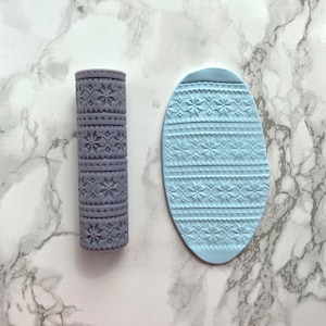 May include: Two silicone rolling pins with a snowflake pattern. One is a traditional rolling pin shape and the other is an oval shape.